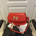 Minimalist red crossbody bag with a golden metal bow buckle and textured leather finish - Red