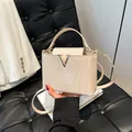 Chic cream crocodile pattern tote bag with silver V buckle on a luxury sofa setting - Beige