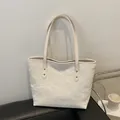Modern ivory tote bag with pleated texture and golden rivets shown on a leather surface - White
