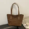 Brown vintage tote bag with paper-like texture and gold rivets on black leather sofa - Brown