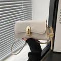 Bolso baguette minimalista crema con hebilla dorada, llevado por una modelo en entorno moderno - Blanco