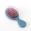 Mini-Massagebürste mit blauem Griff, braunem Kissen und rosa Borsten in ovaler Form - Glänzend Nebelblau