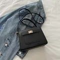 Elegant black crossbody bag with gold hardware on denim jacket and white linen - Black