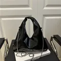 Glänzende schwarze Achseltasche mit Knotengriff und Silberkette auf Buch - Schwarz