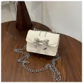 Mini cream crossbody bag with silver bow accent and chain strap on a wooden desk - Off White