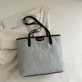 Sac fourre-tout gris argenté avec texture plissée et anses noires sur fond beige - Gris