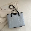 Sac fourre-tout plissé bleu clair avec anses noires posé sur une veste beige - Bleu