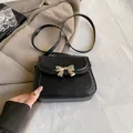 Black leather crossbody bag with elegant gold bow clasp and sleek matte finish - Black
