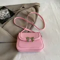 Elegant cherry pink crossbody bag with gold bow clasp on a brown blazer setting - Pink