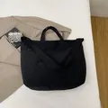 Minimalist large black tote bag in matte nylon shown on bed with aesthetic background - Black