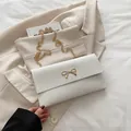 Elegant white envelope shoulder bag with golden bow and chain on beige blazer - White