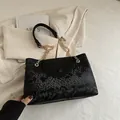 Elegant black snake pattern tote bag with gold chain strap on beige blazer - Black