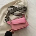 Pink textured square crossbody bag with a wide geometric woven strap and gold lettering - Pink