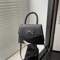 Elegant black square crossbody bag with gold bow clasp and matte leather finish - Black