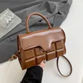 Brown chocolate-textured top handle handbag with crossbody strap on a minimalist desk - Brown