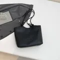 Minimalist black tote bag with rope straps and gold tips on office suit background - Black