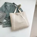 Beige gewebte Stroh-Shopper-Tasche mit weißer Quaste vor modischem Hintergrund - Cremeweiß mit Anhänger