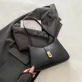 Chic black crescent underarm bag with a golden metal twist lock on grey blazer - Black
