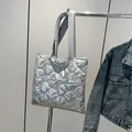 Quilted silver tote bag in puffer style with grey handles hanging on a metal stand - Silver