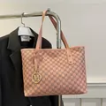 Pink tote bag with monogram pattern and gold M charm hanging on a metal display stand - Pink