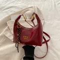 Bolso de media luna rojo oscuro en piel brillante con logo dorado y colgante tejido - Con Colgante / Rojo