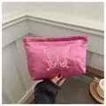 Détail d'une trousse de maquillage en satin rose avec broderie papillon et texture soyeuse - Rose rose