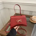 Red bow fashion handbag with gold buckle, featuring versatile top handle and crossbody strap - Red