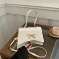 Elegant cream white crossbody bag with golden bow hardware and top handle design - White