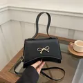Elegant black trapezoid handbag with a gold bow buckle and adjustable shoulder strap - Black
