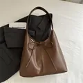 Brown leather tote bag with elegant bow detail on a grey suit jacket background - Brown