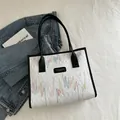 White faux leather tote bag featuring colorful embroidery and black contrast handles - White