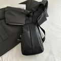 Elegante bolso bandolera plisado negro sobre chaqueta gris con un libro - Negro