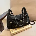 Borsa tote nera con ciondoli a farfalla argentati e tracolla a catena su sedia beige - Senza Ciondolo / Nero