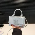Metallisch silberne Handtasche mit Krokostruktur und Metallschnalle in der Hand - Silber