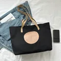 Schwarze Canvas-Tragetasche mit rosa Logo und braunen Lederriemen auf weißem Stoff - Schwarz