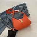 Borsa a mezzaluna arancione vivace con chiusura metallica dorata su sfondo in denim - Arancione