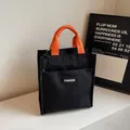 Black waterproof tote lunch bag with orange handles and fashion label detail - Black
