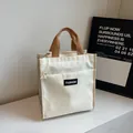 Cream-colored canvas lunch bag with brown woven handles and a front zipper pocket - Off White