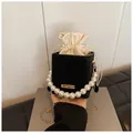 Macro detail of black suede bucket bag with oversized pearl handle and gold chain - Black