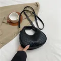 Chic black woven crescent handbag with gold hardware and adjustable strap in a lifestyle setting - Black