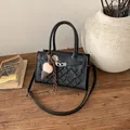 Chic black crossbody bag with vintage floral embossing and plush pendant on wooden table - Black With Rabbit Pendant