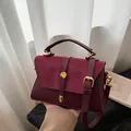 Elegant burgundy leather handbag with gold buckle and suede detail, shown held by hand - Burgundy