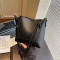 Dettaglio della borsa a secchiello in pelle nera con cuciture fini vicino al laptop - Nero