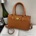 Bolso elegante de cuero marrón con hebilla de corazón dorada sobre un libro abierto - Marrón