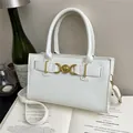 Elegante bolso de mano en cuero blanco con cierre de corazón dorado sobre un libro - Blanco