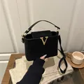 Sac seau élégant en daim noir avec fermoir en V doré posé sur un bureau en bois - Noir