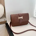 Braided caramel brown crossbody bag with gold H-buckle in a minimalist studio setting - Brown