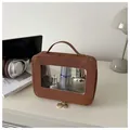 Detail of a brown textured makeup bag with a large transparent window and gold zippers - Brown