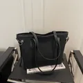 Matte black leather tote bag with gold ring detail on a minimalist black chair - No Pendant / Black