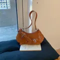 Minimalist tan crescent shoulder bag with metallic buckles and animal charm on a book - Brown